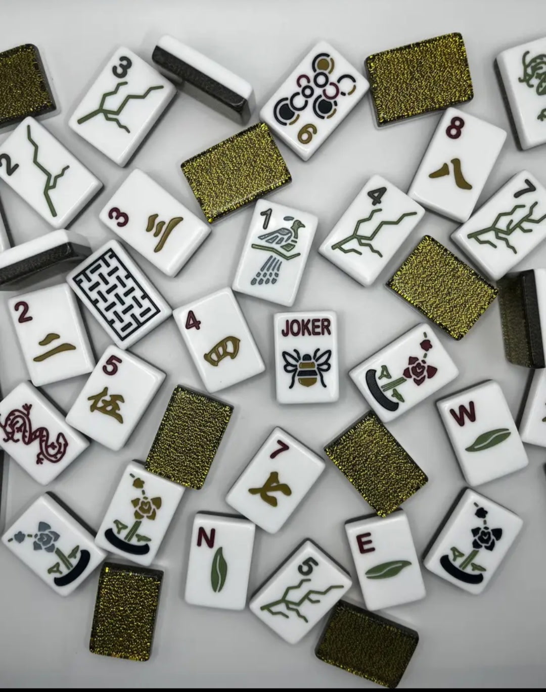 Scattered white Mahjong tiles with botanical symbols and black-and-gold glitter backs