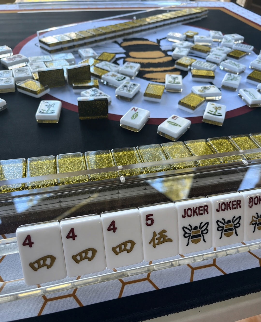 Gold glitter-backed Mahjong tiles and clear racks arranged on a game mat during play